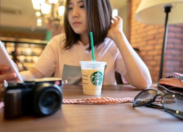 starbucks drinks for kids: young girl drinking an iced starbucks drink at a cafe