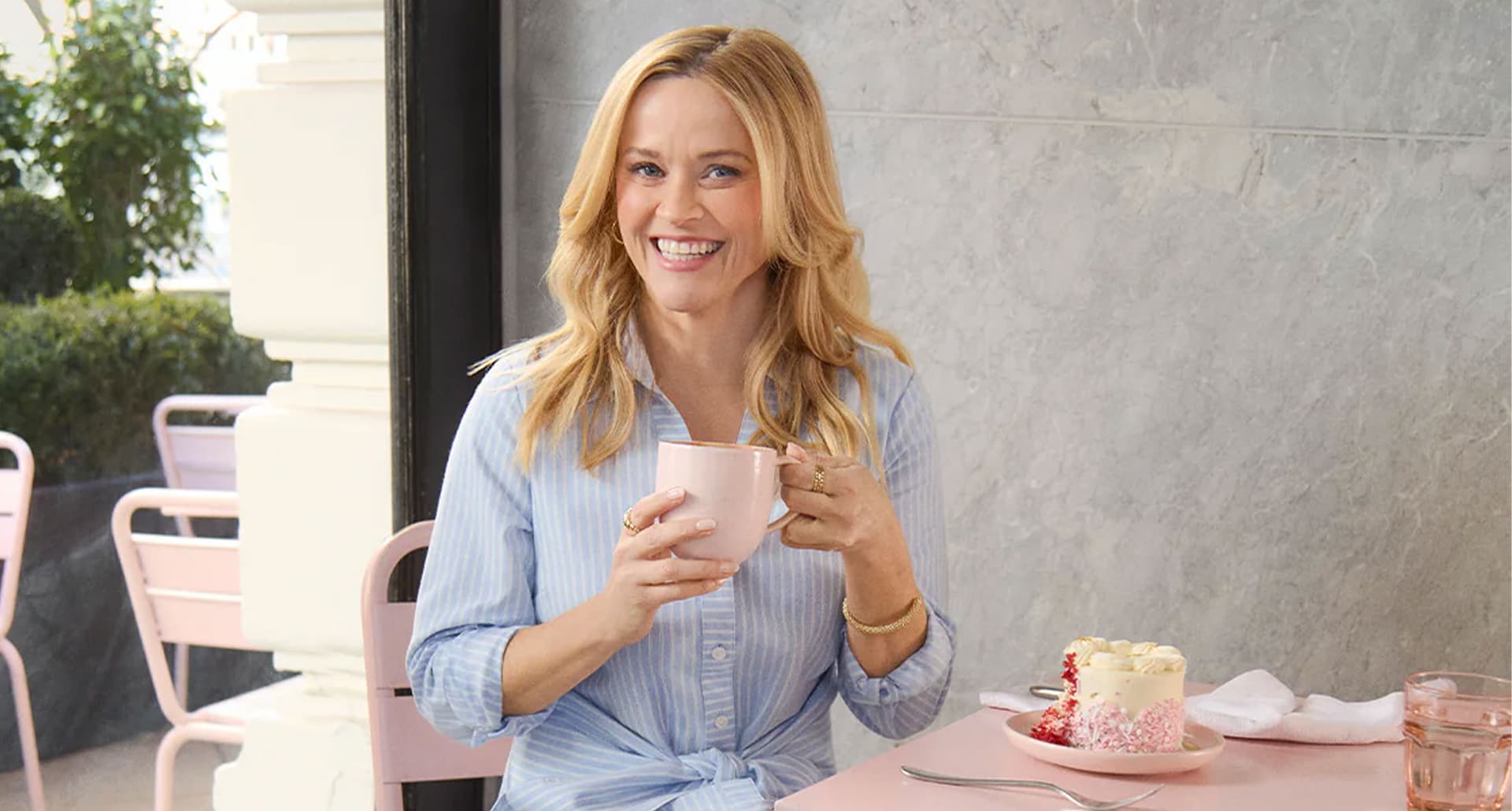 reese-witherspoon-birthday-shirtdress: A photo of Reese Witherspoon in a blue and white pinstripe dress while smiling and sipping from a white mug.